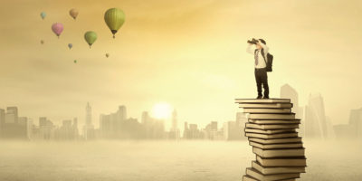 little boy standing on a pile of books looking out over the world and dreaming of adventures
