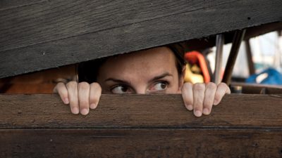 a woman peeking out of an old, wooden fence as if she's playing hide and seek