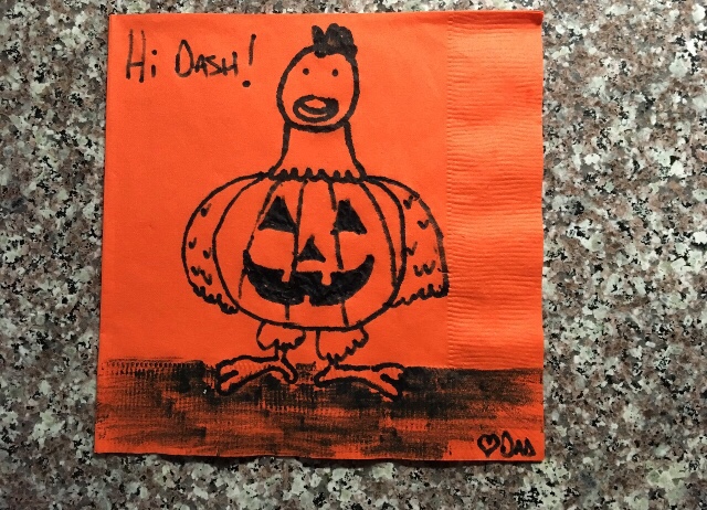 A chicken dressed up like a pumpkin drawn in black marker on an orange napkin.
